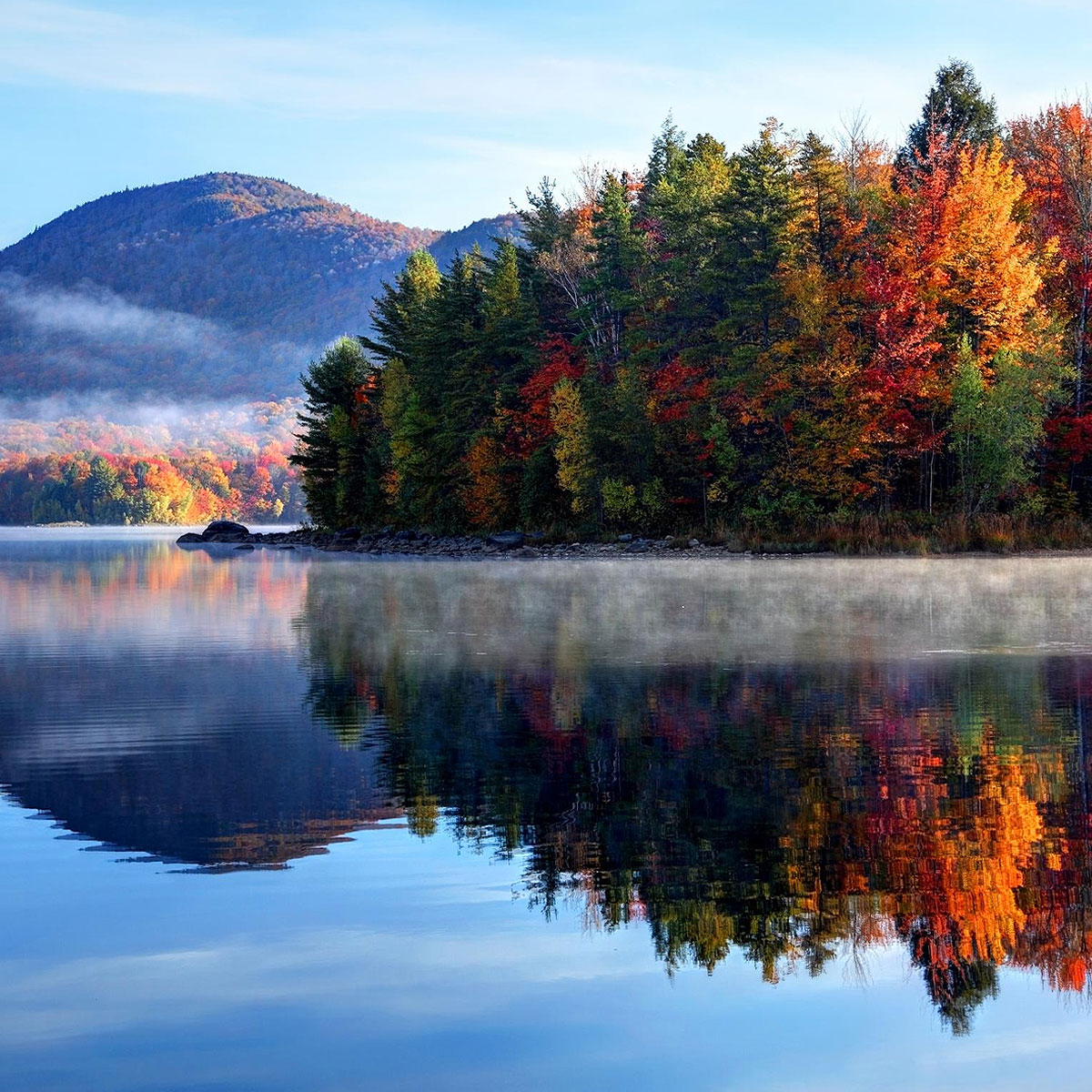 Experience the serene beauty of autumn reflected in the lake, amidst a landscape of fallen leaves and forest trees.