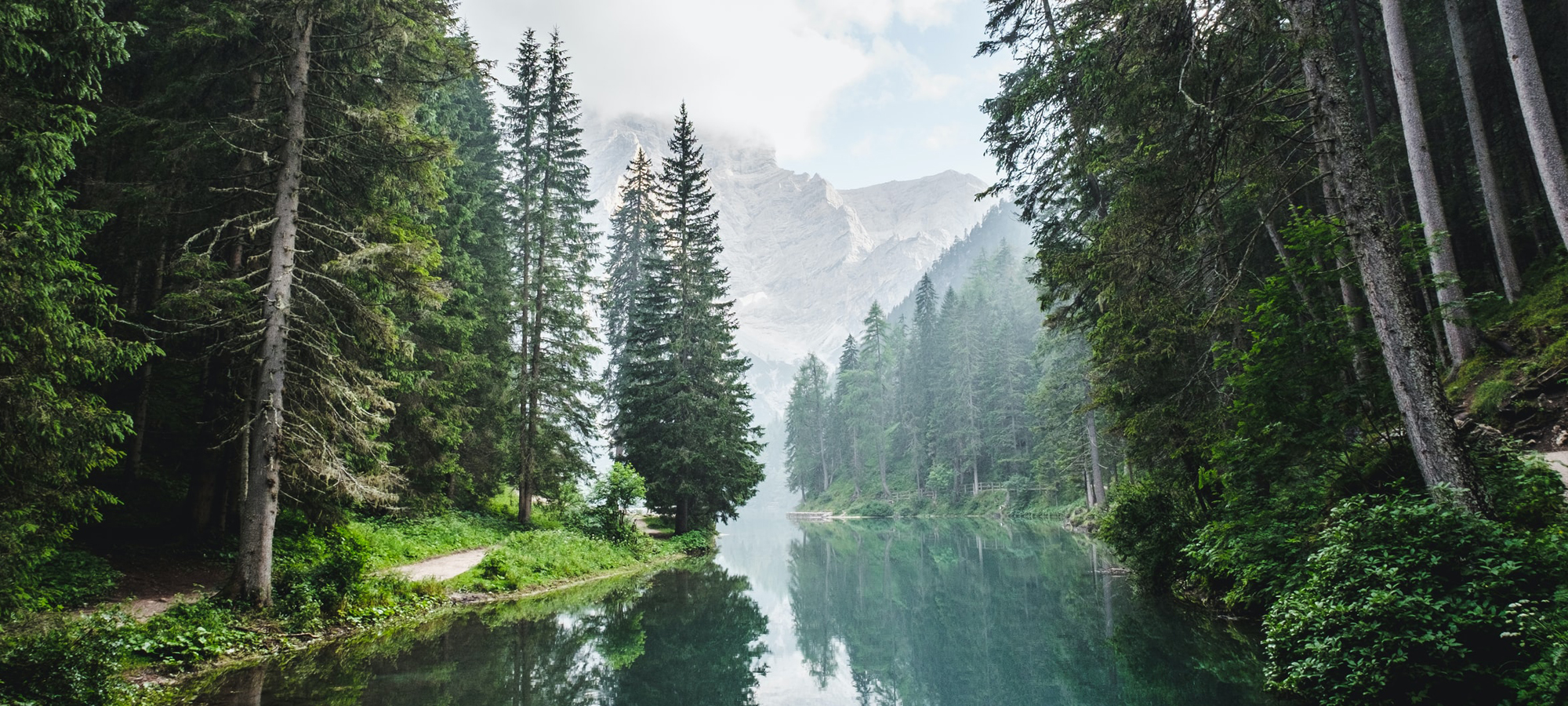 Experience the serene beauty of nature with this landscape featuring mountains, forests, a tranquil river, and a vivid sky.